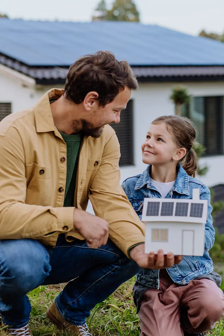 Vater und Tochter hocken vor einem Haus mit PV Anlage